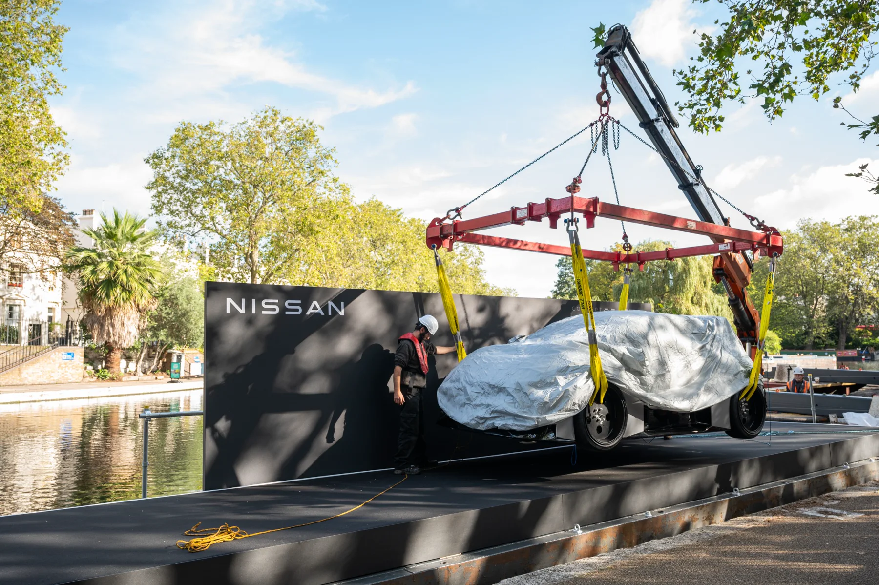 Covered concept car being lifted onto a floating Nissan launch stage