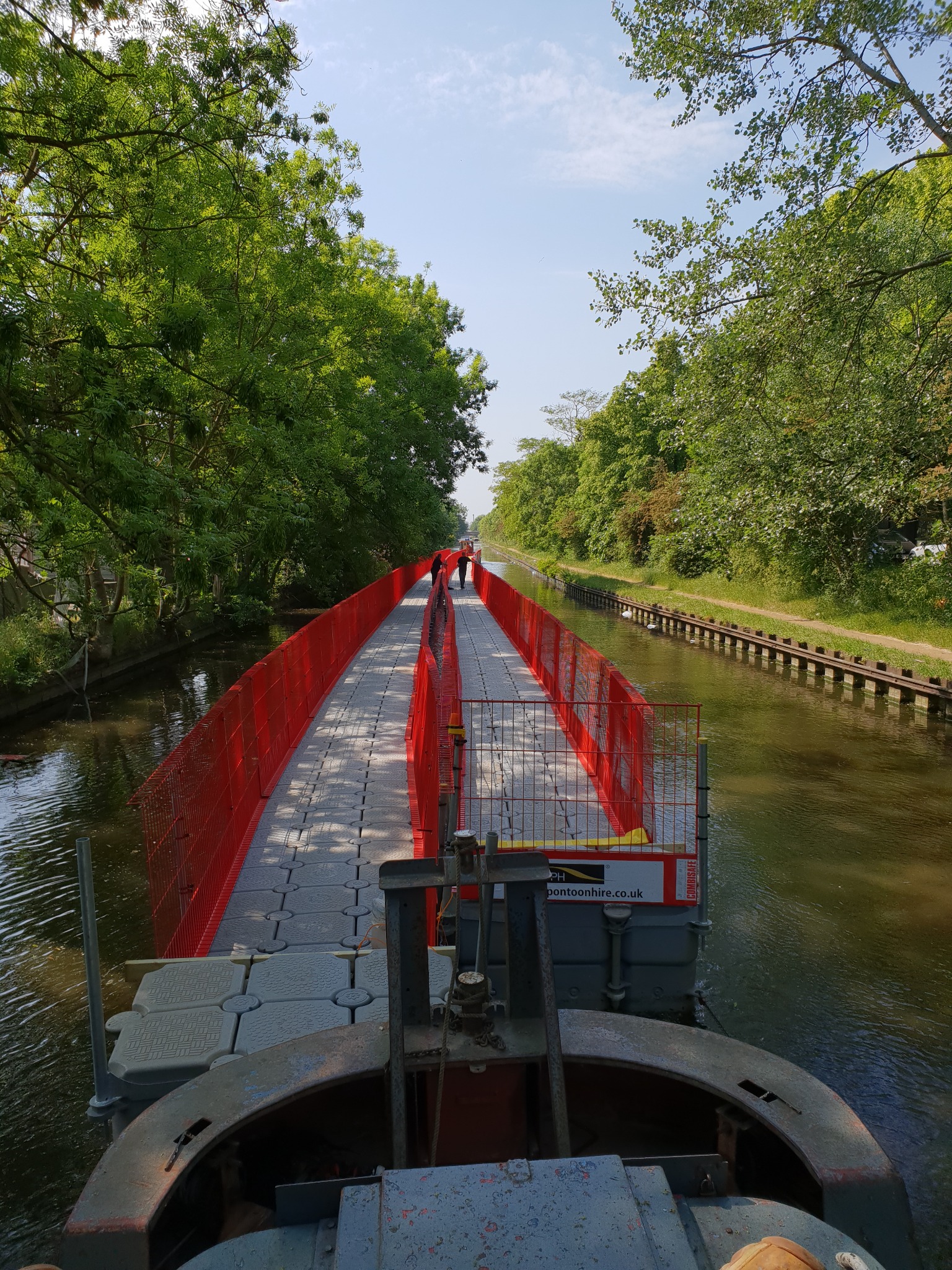 A long modular pontoon work platform being moved along the canal by a WHH tug